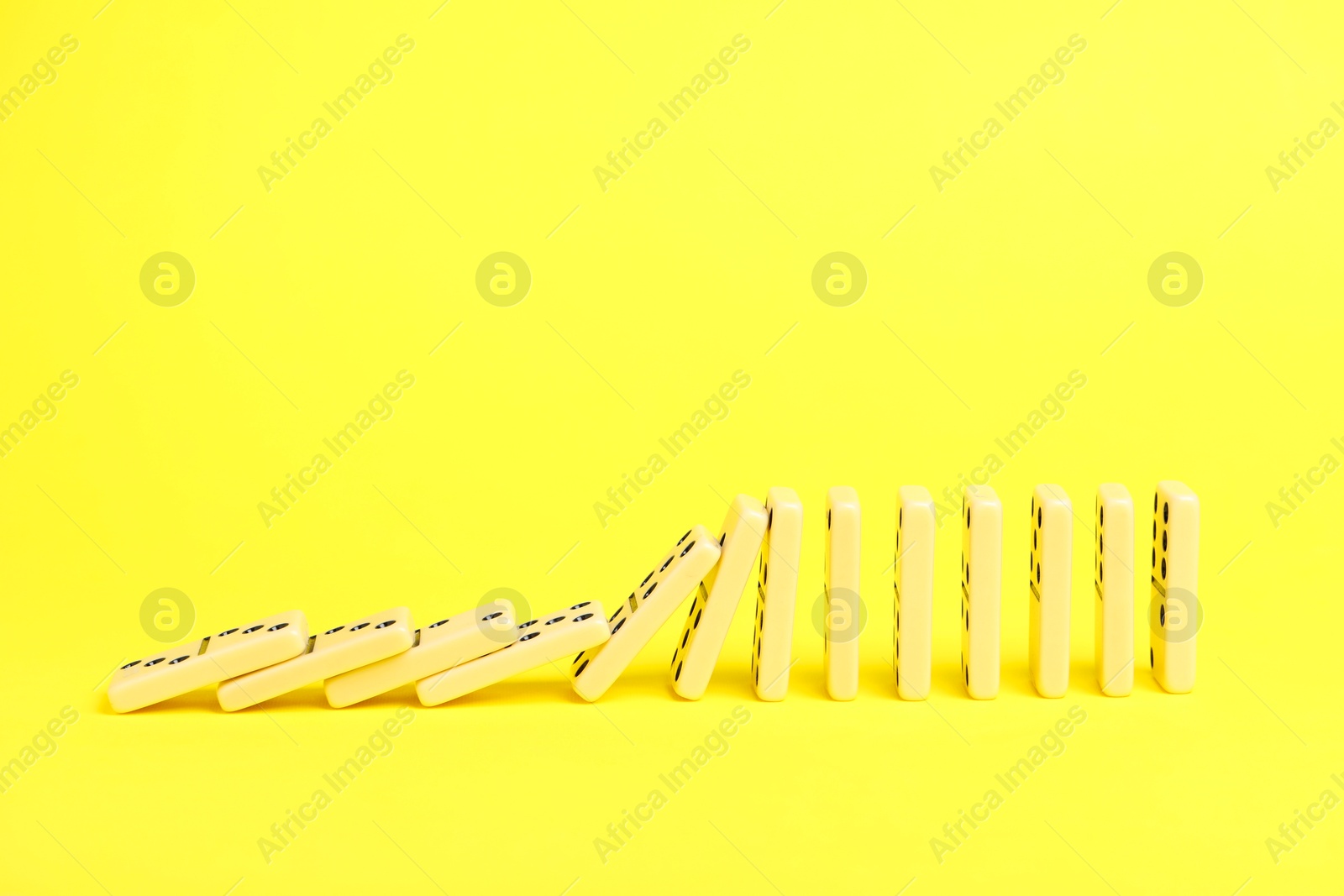 Photo of Domino effect. Tiles falling on yellow background, space for text