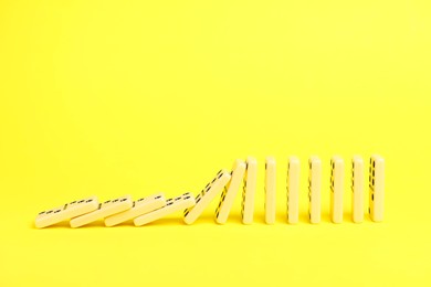 Photo of Domino effect. Tiles falling on yellow background, space for text