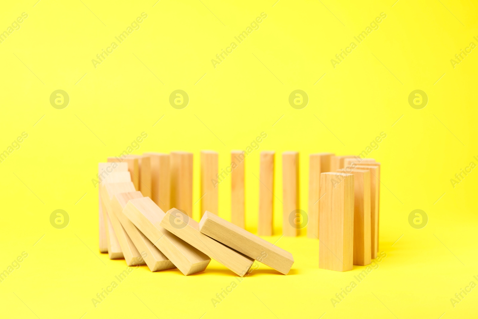 Photo of Domino effect. Wooden blocks falling on yellow background