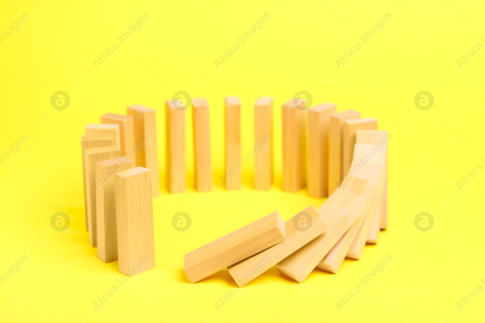 Photo of Domino effect. Wooden blocks falling on yellow background