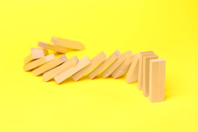 Photo of Domino effect. Wooden blocks falling on yellow background