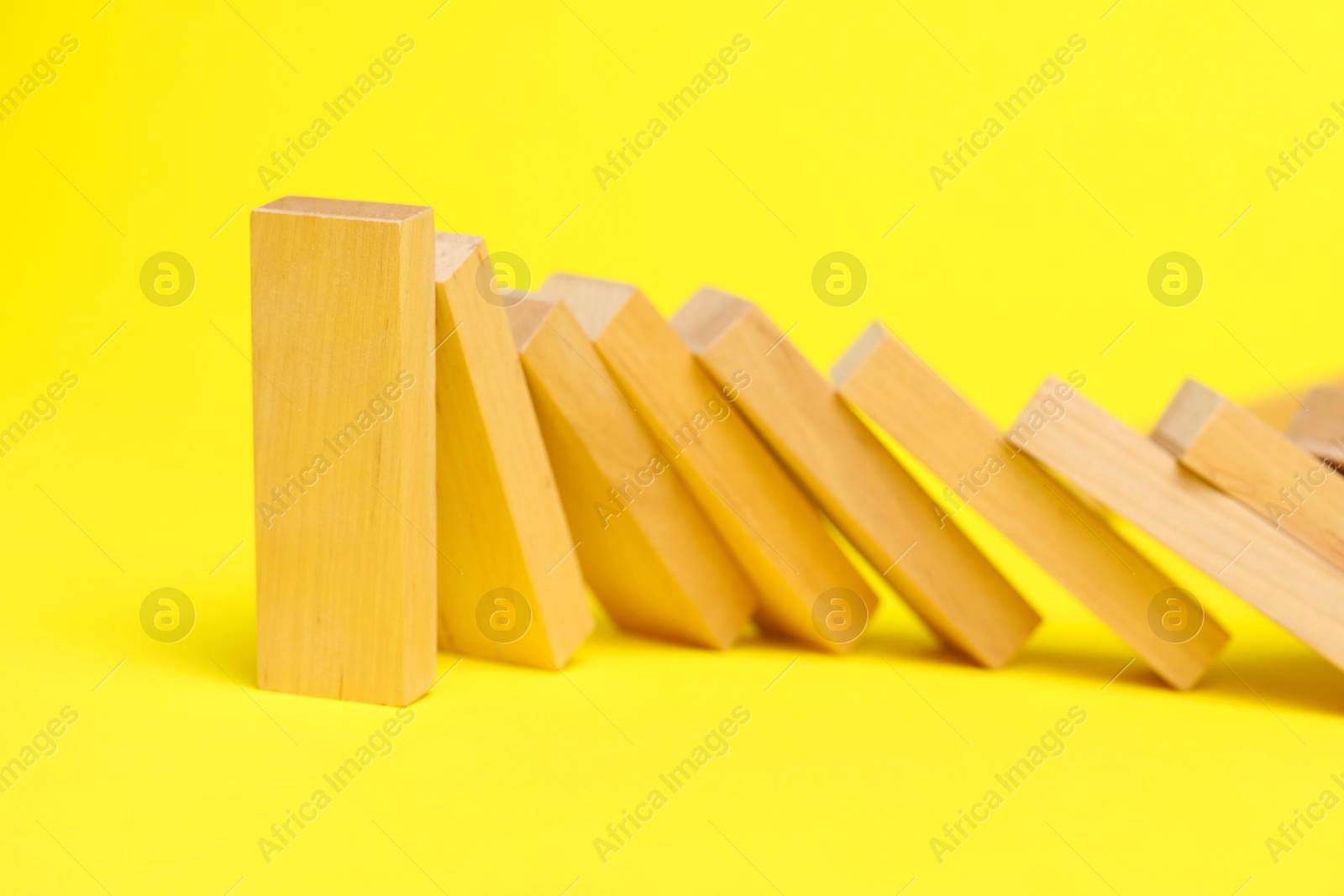 Photo of Domino effect. Wooden blocks falling on yellow background, closeup