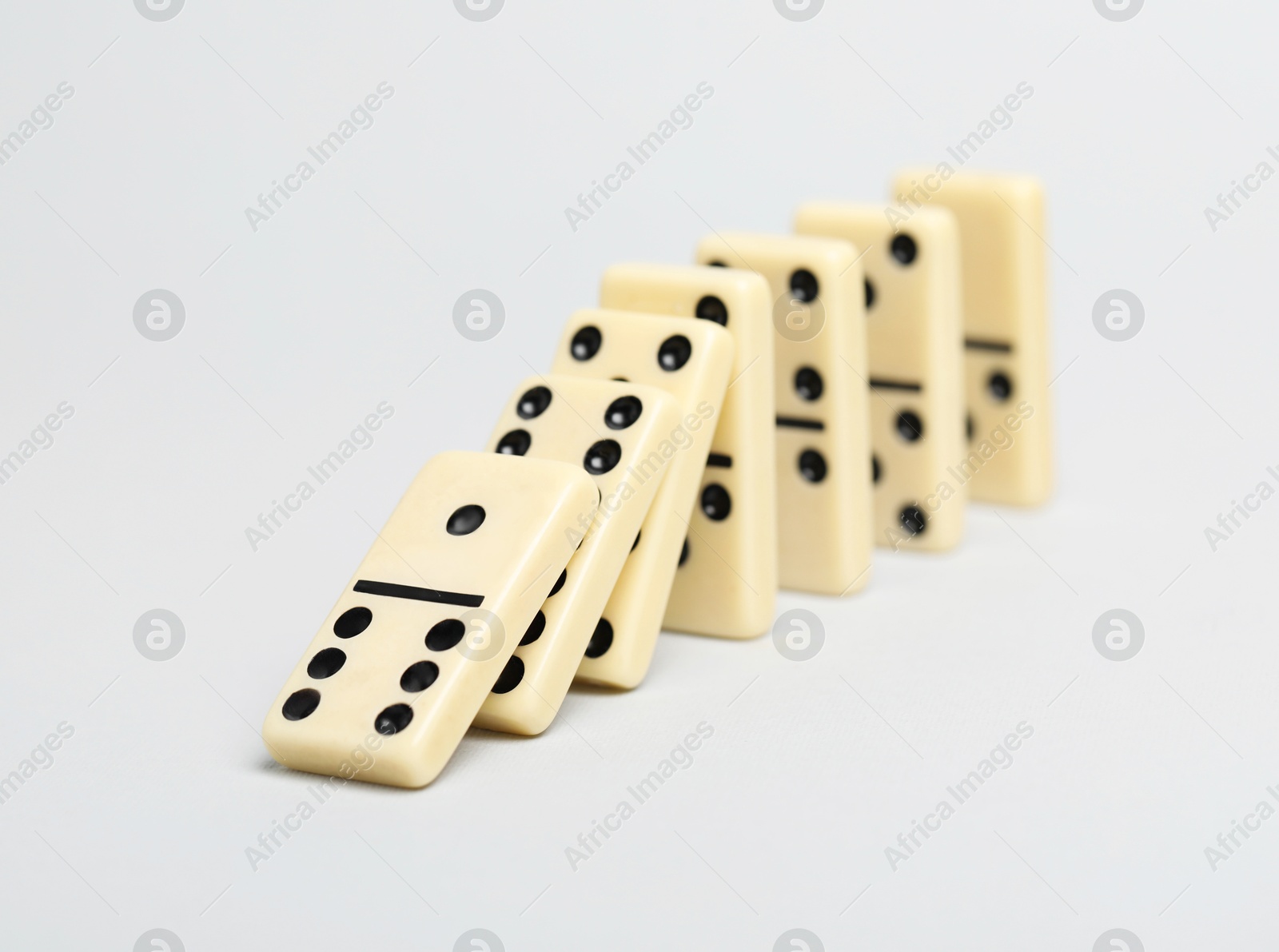 Photo of Domino effect. Tiles falling on light background