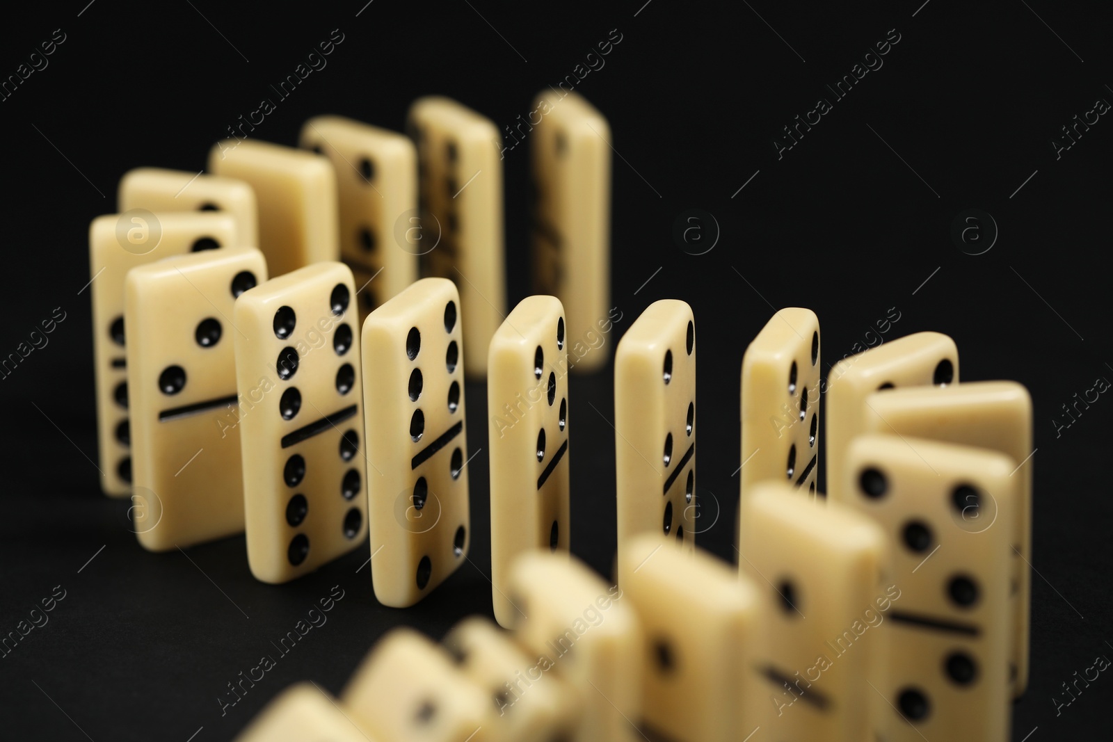 Photo of Domino effect. Tiles falling on black background, closeup