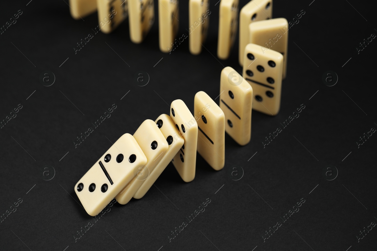 Photo of Domino effect. Tiles falling on black background