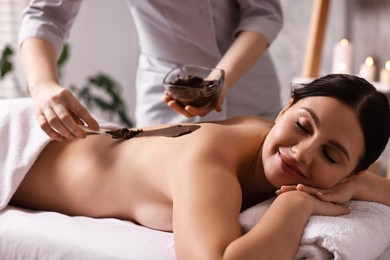 Chocolate body wrap. Spa worker applying mask onto woman's back in salon, closeup