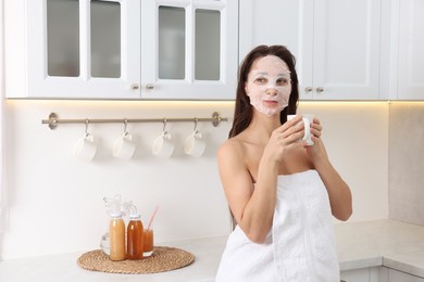 Spa day. Beautiful woman with face mask and cup of drink in kitchen