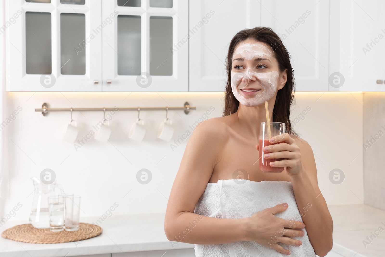 Photo of Spa day. Beautiful woman with face mask and juice in kitchen, space for text