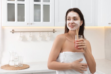 Spa day. Beautiful woman with face mask and juice in kitchen, space for text