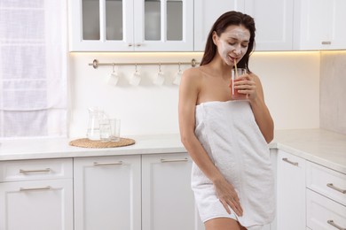 Spa day. Beautiful woman with face mask drinking juice in kitchen, space for text