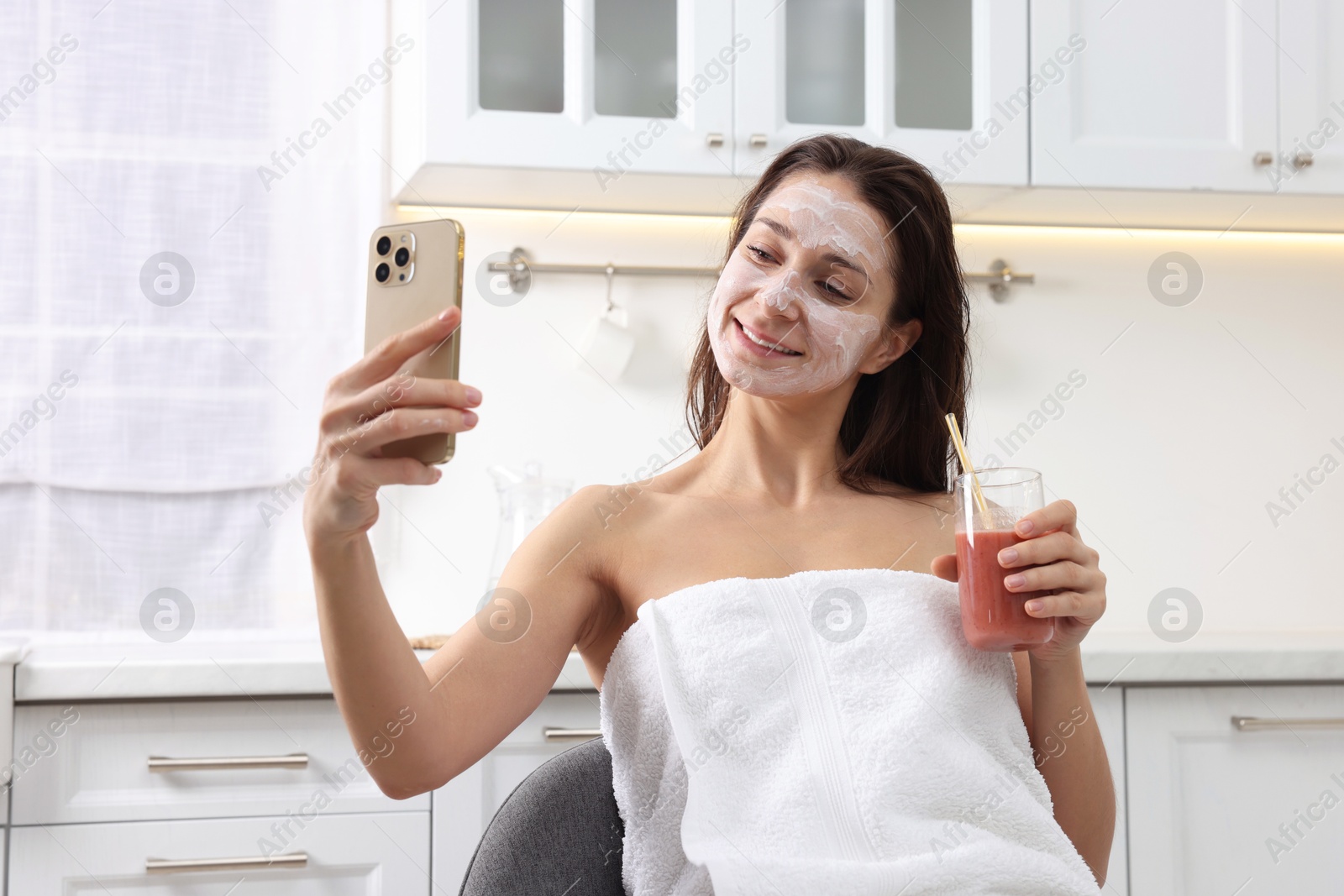 Photo of Spa day. Beautiful woman with face mask and juice taking selfie in kitchen