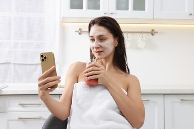 Photo of Spa day. Beautiful woman with face mask and juice using smartphone in kitchen