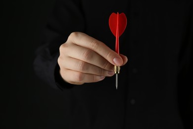 Photo of Woman holding dart on black background, closeup