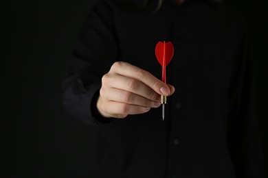 Photo of Woman holding dart on black background, closeup