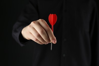 Photo of Woman holding dart on black background, closeup