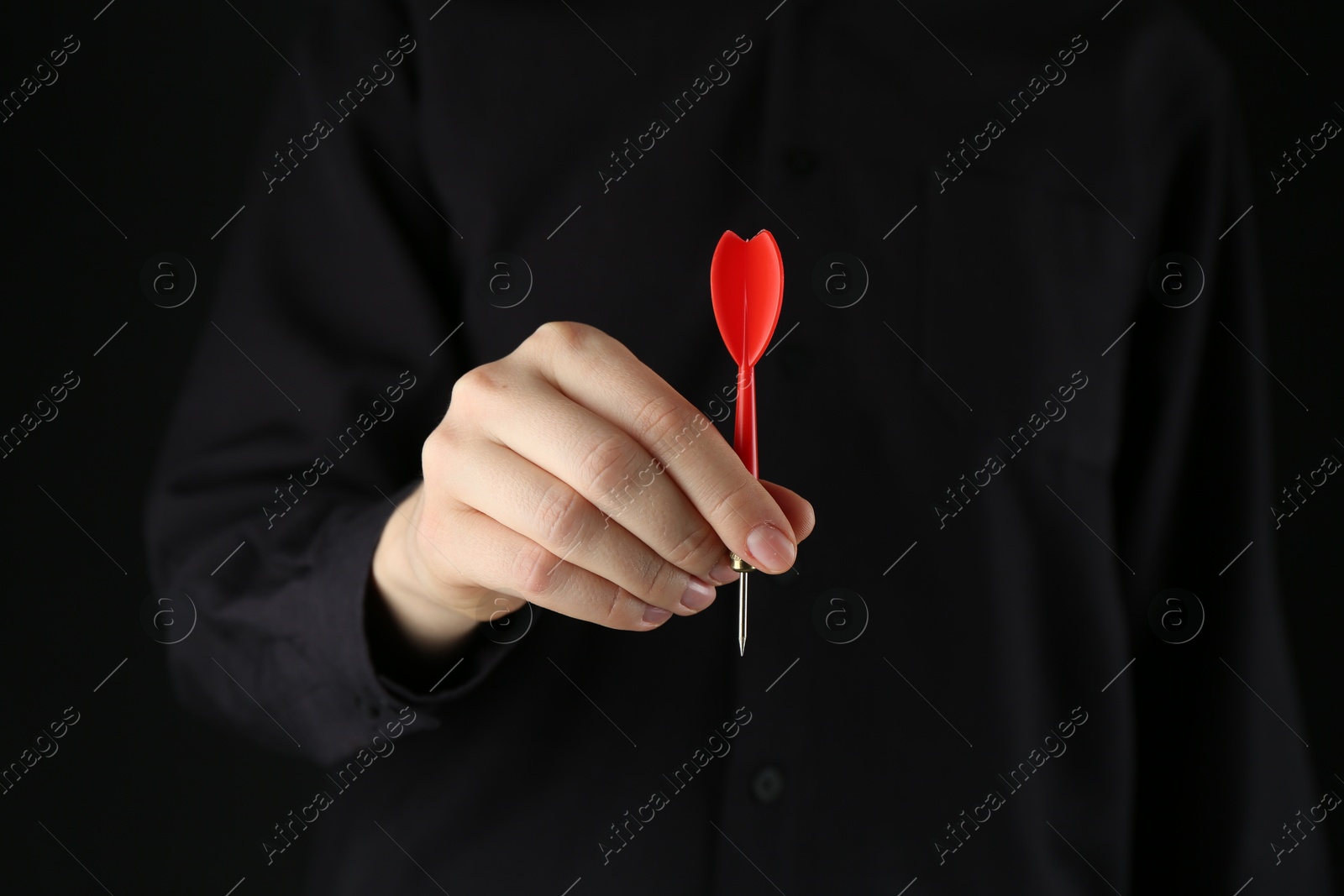 Photo of Woman holding dart on black background, closeup