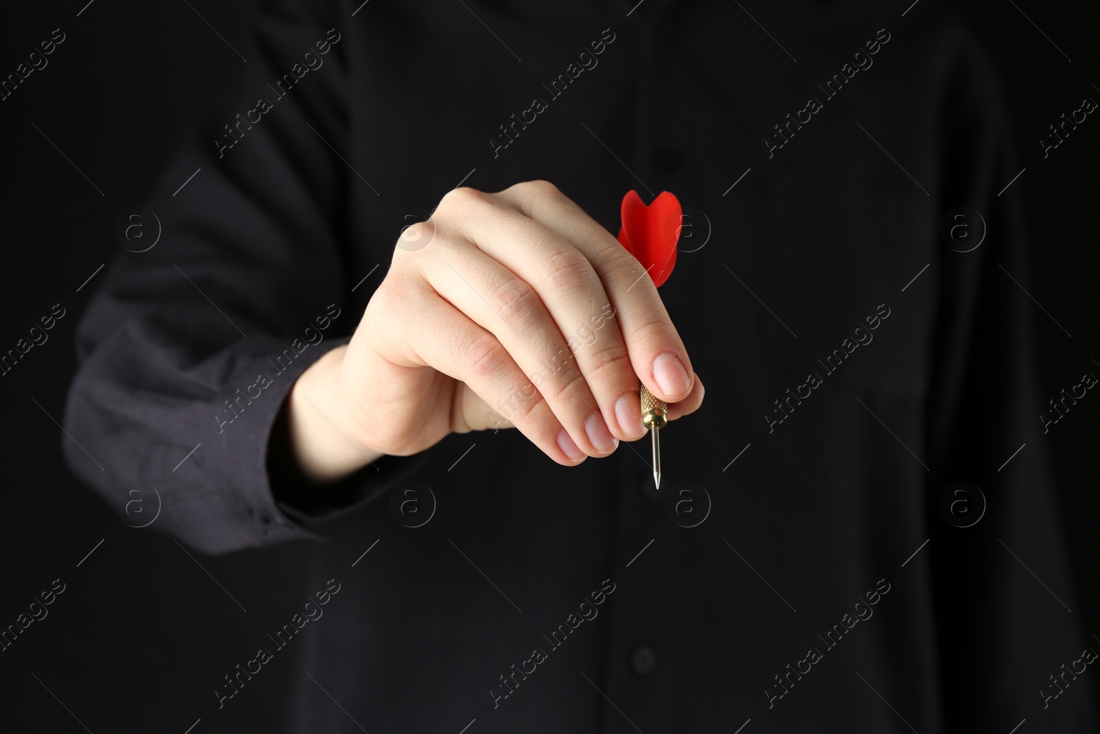 Photo of Woman holding dart on black background, closeup