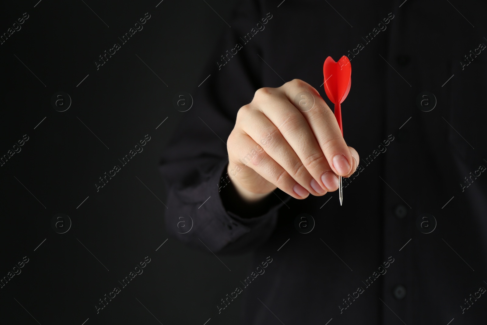 Photo of Woman holding dart on black background, closeup