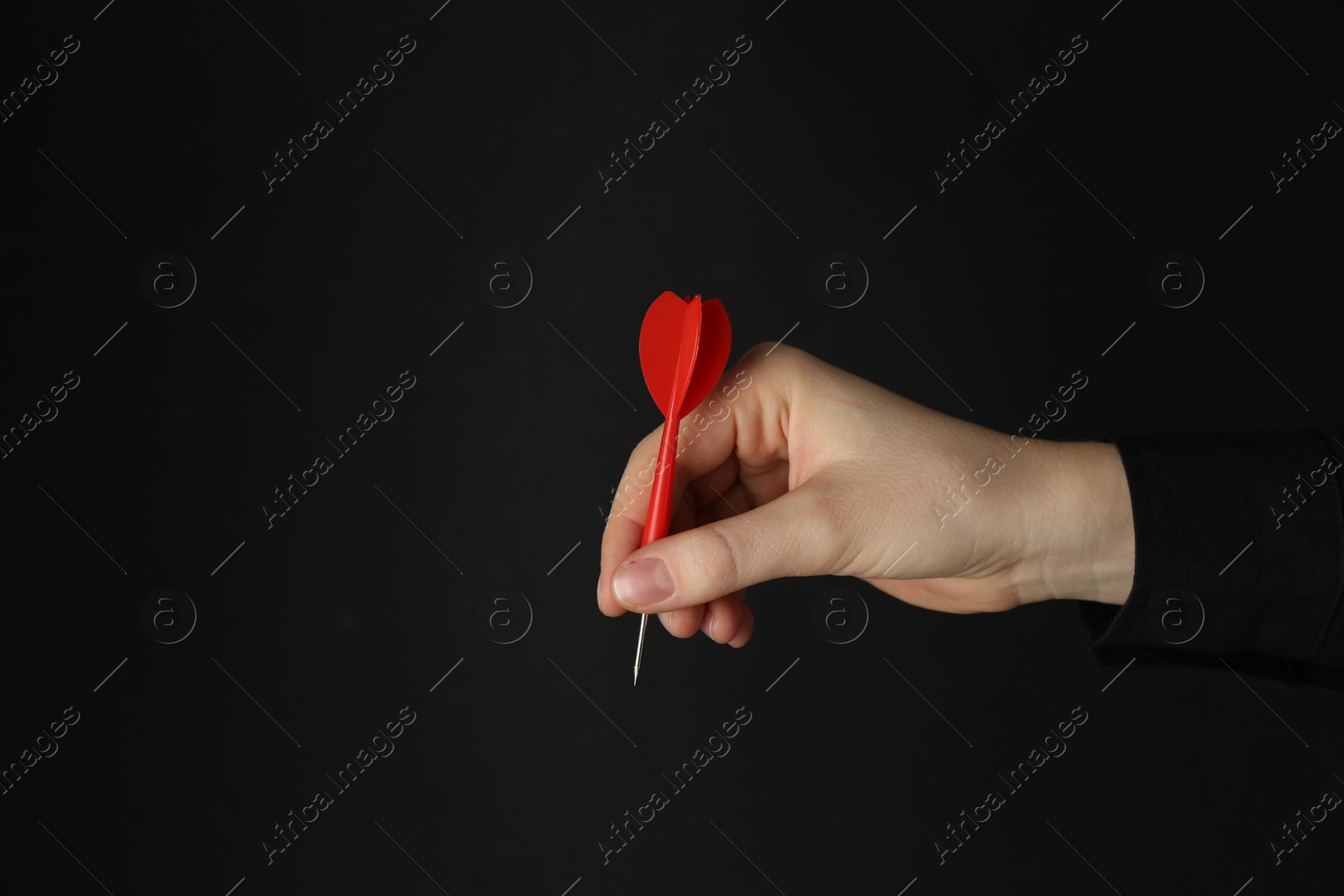 Photo of Woman holding dart on black background, closeup. Space for text