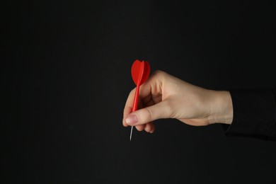 Photo of Woman holding dart on black background, closeup. Space for text