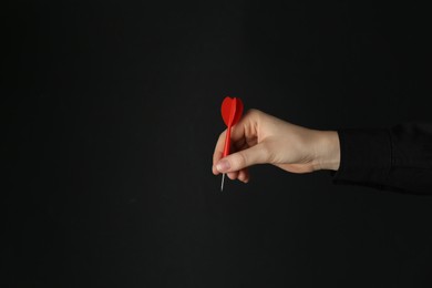 Photo of Woman holding dart on black background, closeup. Space for text