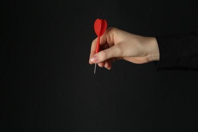 Photo of Woman holding dart on black background, closeup. Space for text