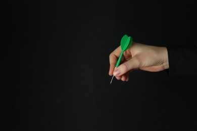 Photo of Woman holding dart on black background, closeup. Space for text