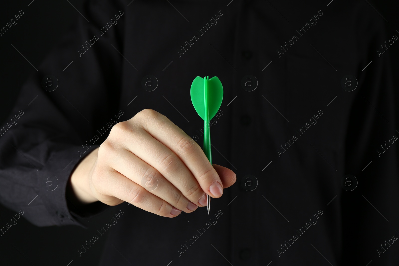 Photo of Woman holding dart on black background, closeup