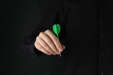 Photo of Woman holding dart on black background, closeup