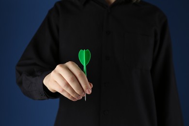 Photo of Woman holding dart on blue background, closeup