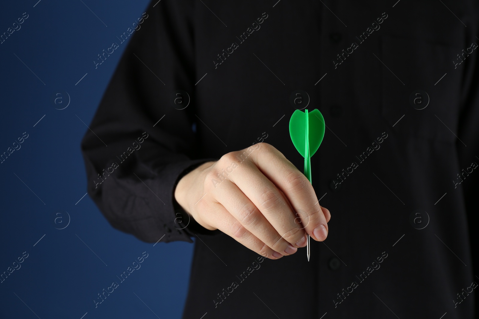 Photo of Woman holding dart on blue background, closeup