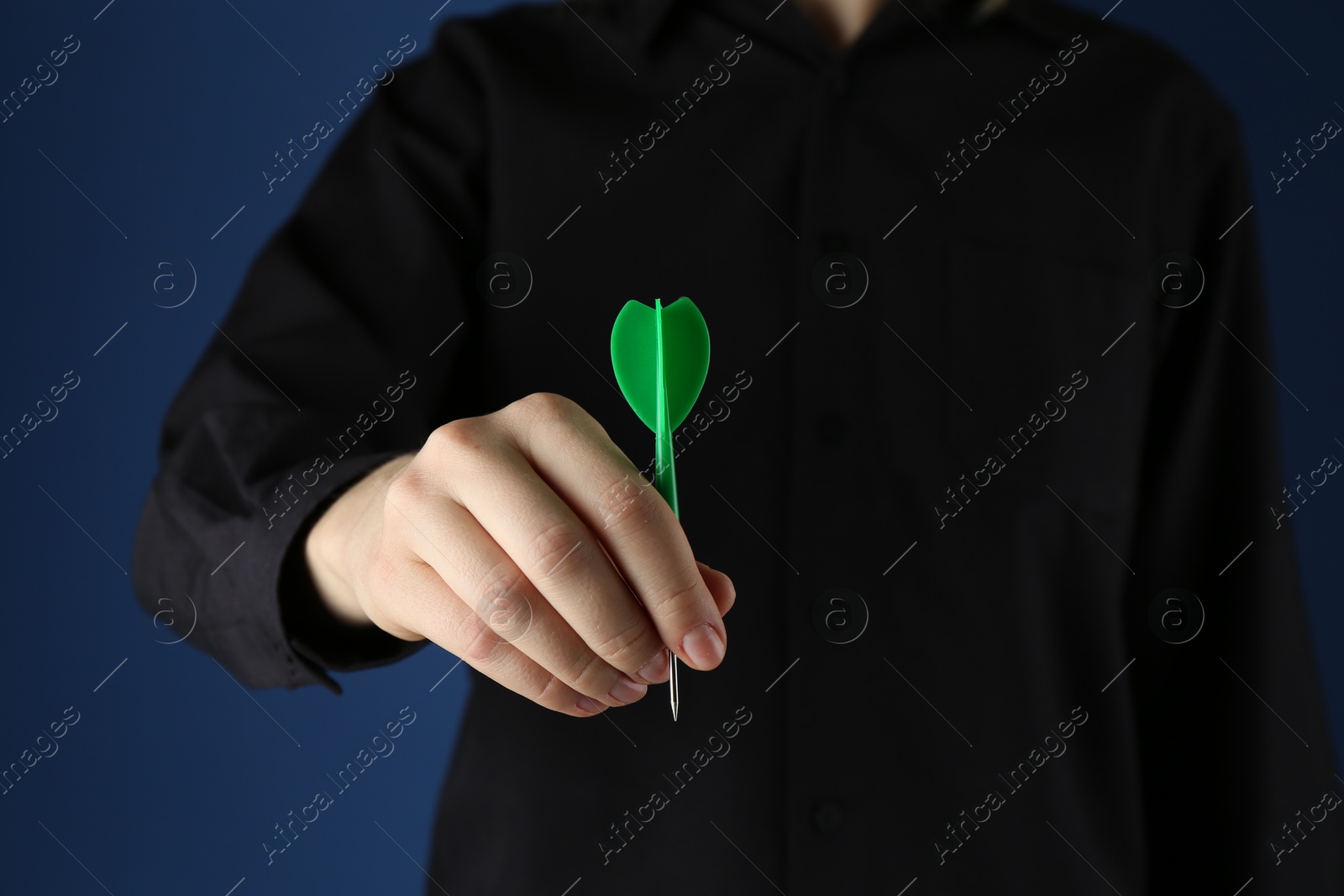 Photo of Woman holding dart on blue background, closeup