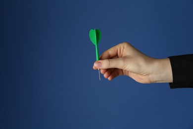 Photo of Woman holding dart on blue background, closeup. Space for text