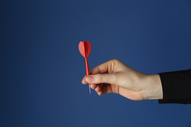 Photo of Woman holding dart on blue background, closeup. Space for text