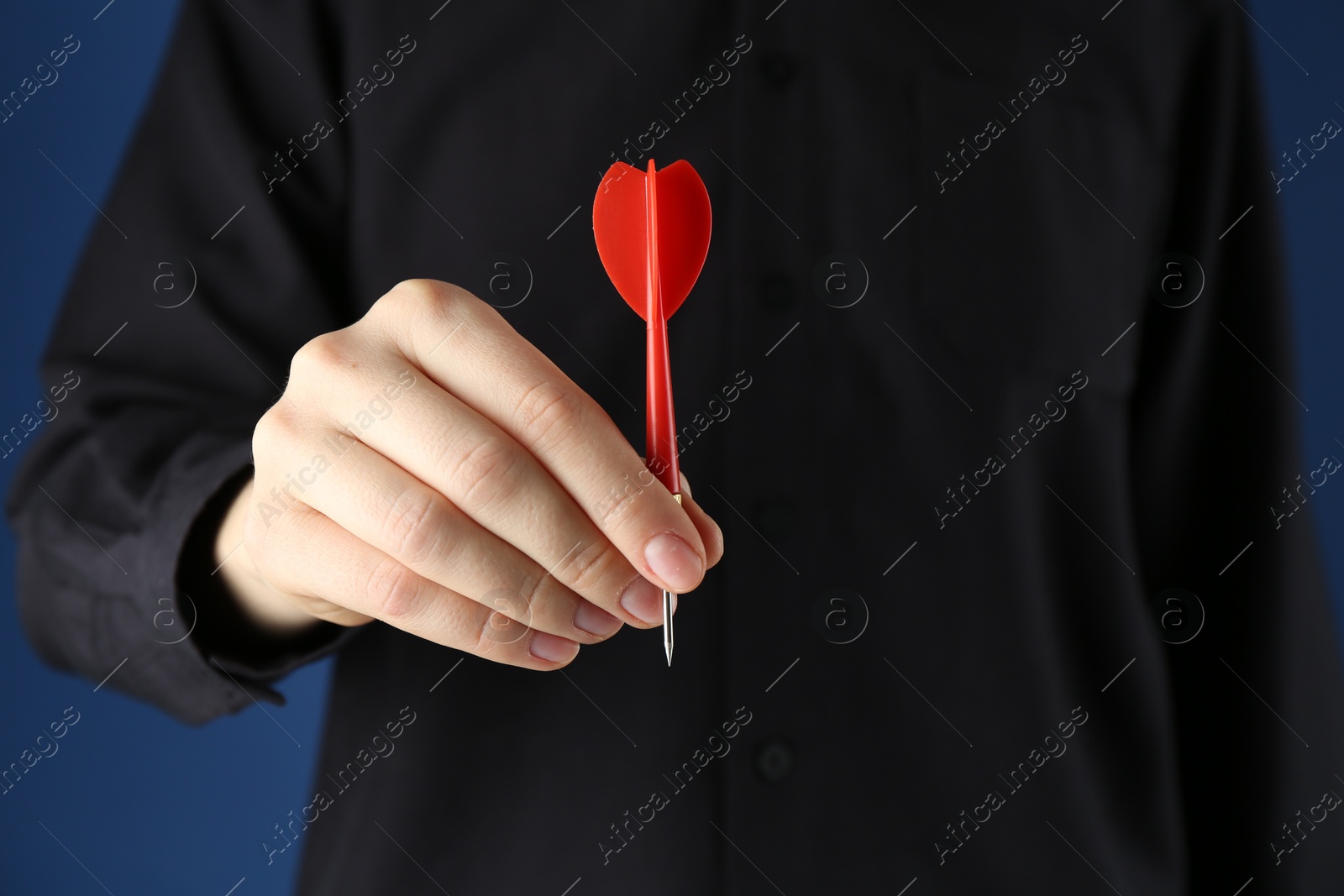 Photo of Woman holding dart on blue background, closeup