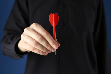 Photo of Woman holding dart on blue background, closeup