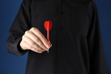 Photo of Woman holding dart on blue background, closeup