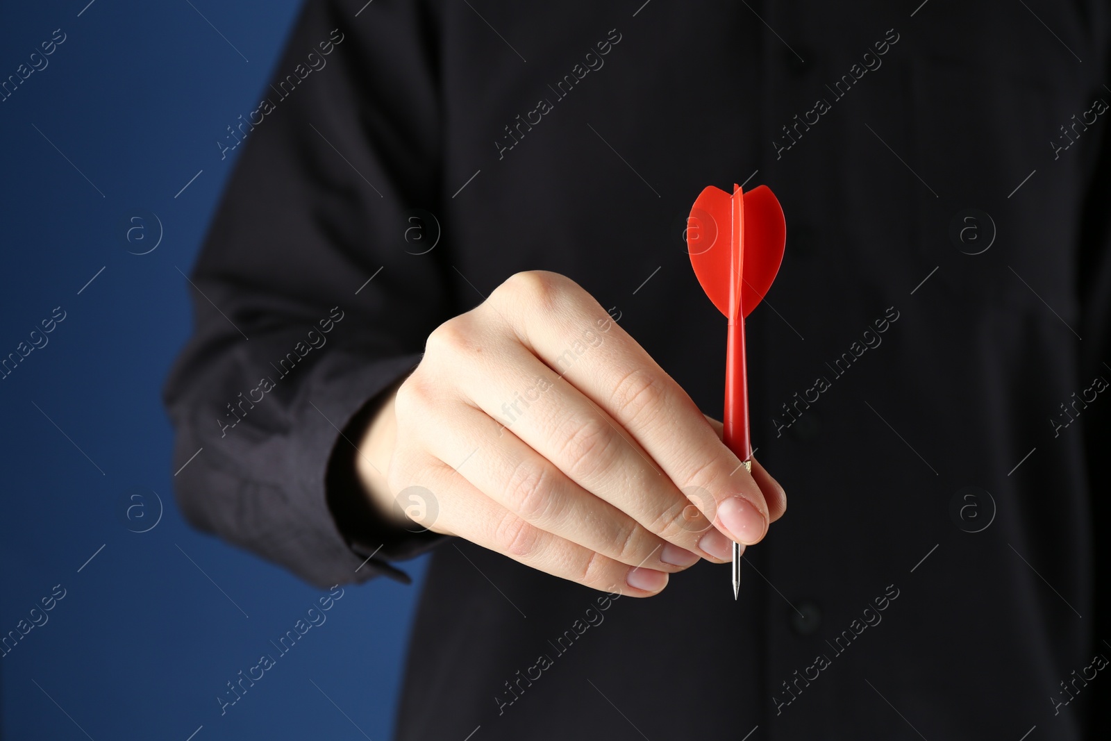 Photo of Woman holding dart on blue background, closeup