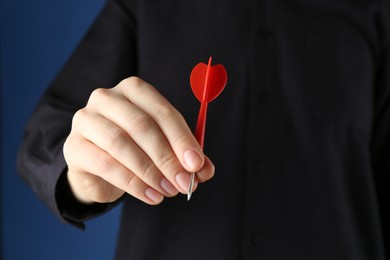 Photo of Woman holding dart on blue background, closeup