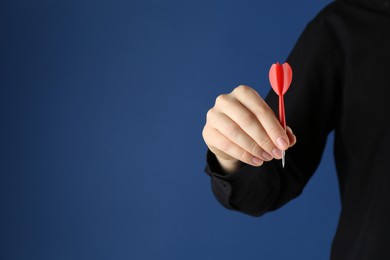 Photo of Woman holding dart on blue background, closeup. Space for text