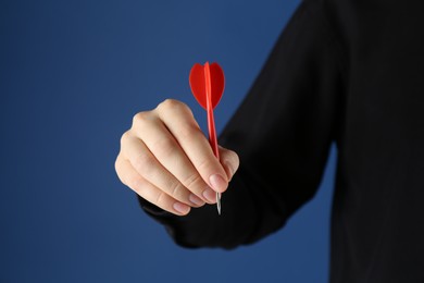 Photo of Woman holding dart on blue background, closeup