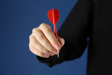 Photo of Woman holding dart on blue background, closeup