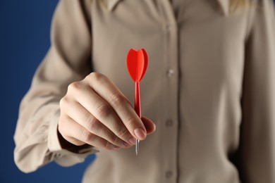 Photo of Woman holding dart on blue background, closeup