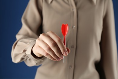 Photo of Woman holding dart on blue background, closeup