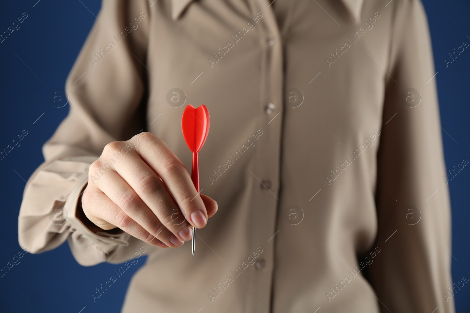 Photo of Woman holding dart on blue background, closeup