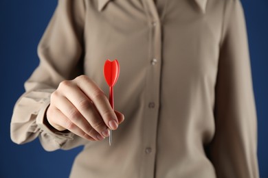 Photo of Woman holding dart on blue background, closeup