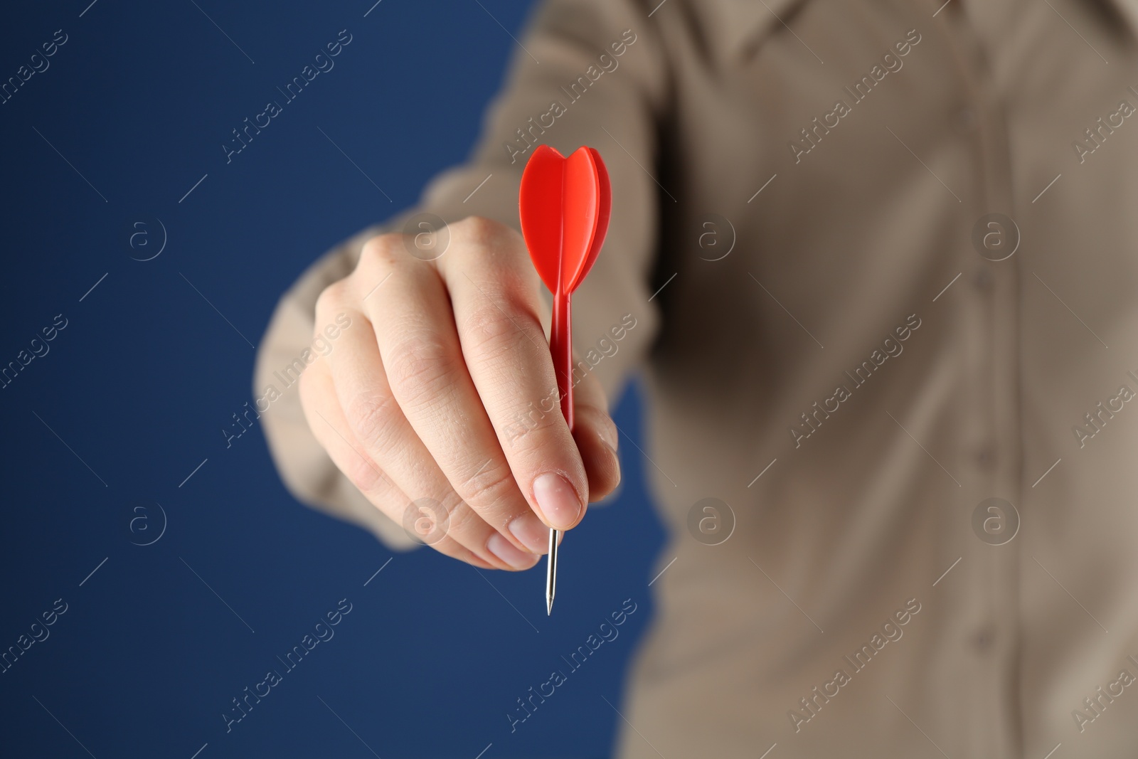 Photo of Woman holding dart on blue background, closeup