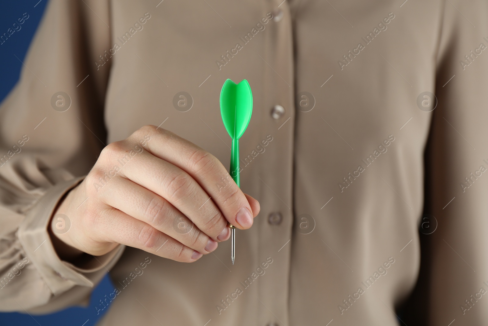 Photo of Woman holding dart on blue background, closeup