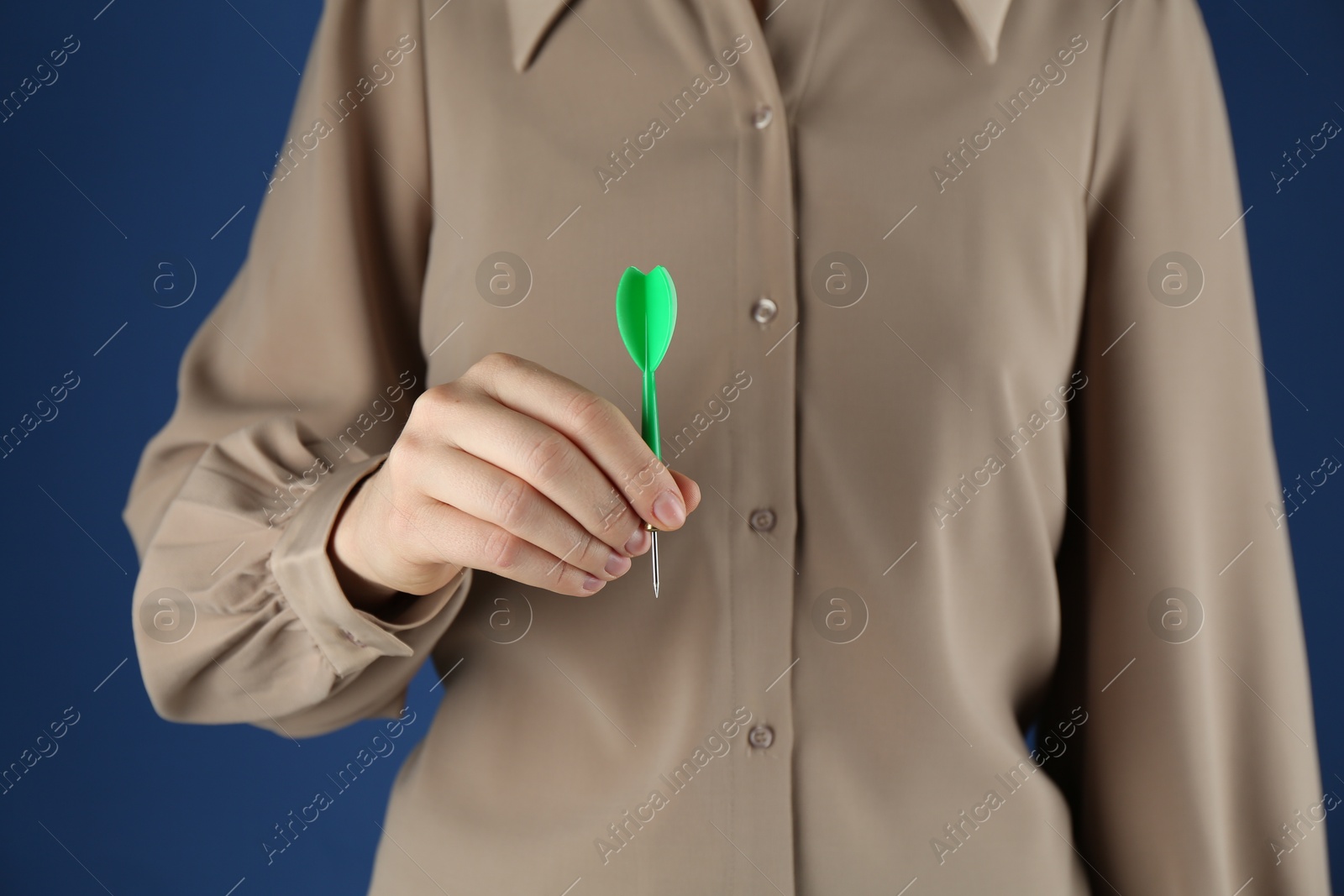 Photo of Woman holding dart on blue background, closeup