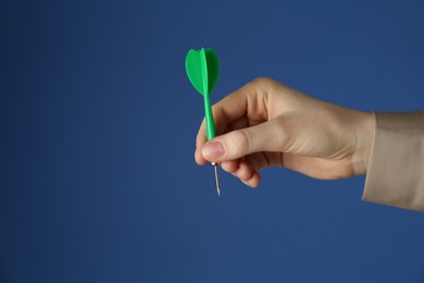 Photo of Woman holding dart on blue background, closeup. Space for text